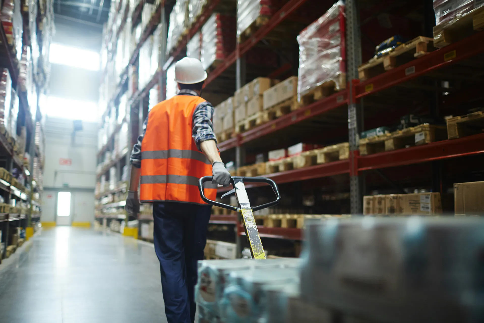 A worker pulls a pallet with packaged items across a warehouse